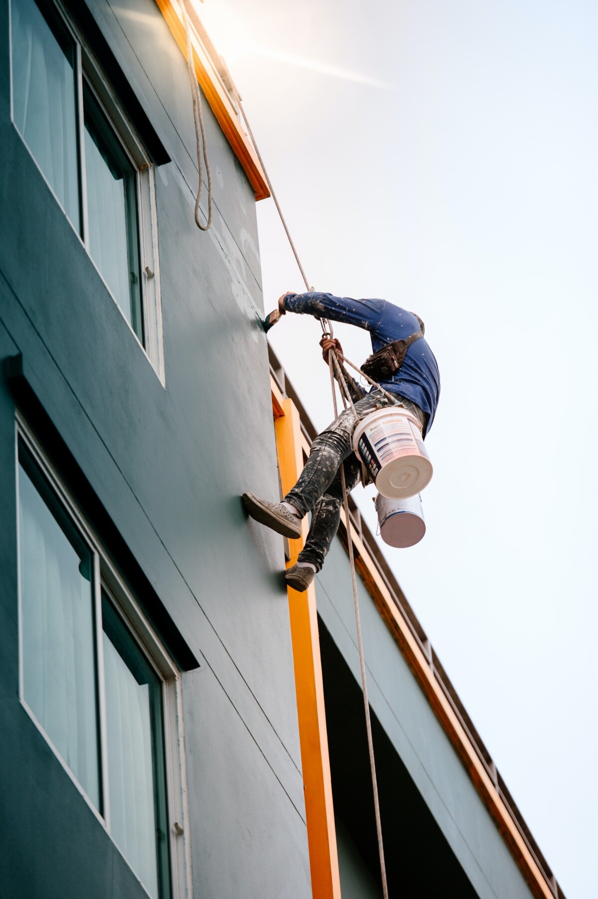 man hanging from rope painting commercial building
