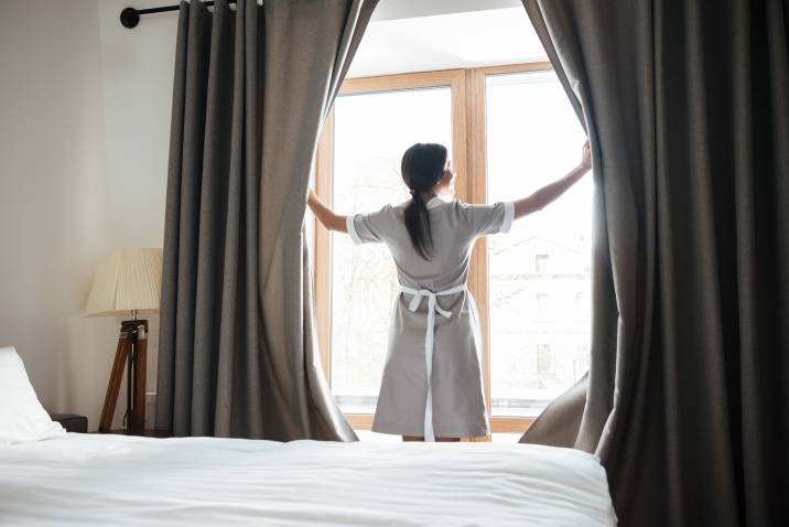 hotel housekeeper opening window curtains and airing out the room