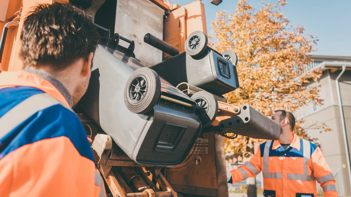 two men emptying trash bins into a truck