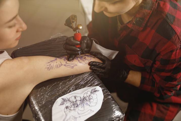 a tattoo artist tattooing a woman's arm