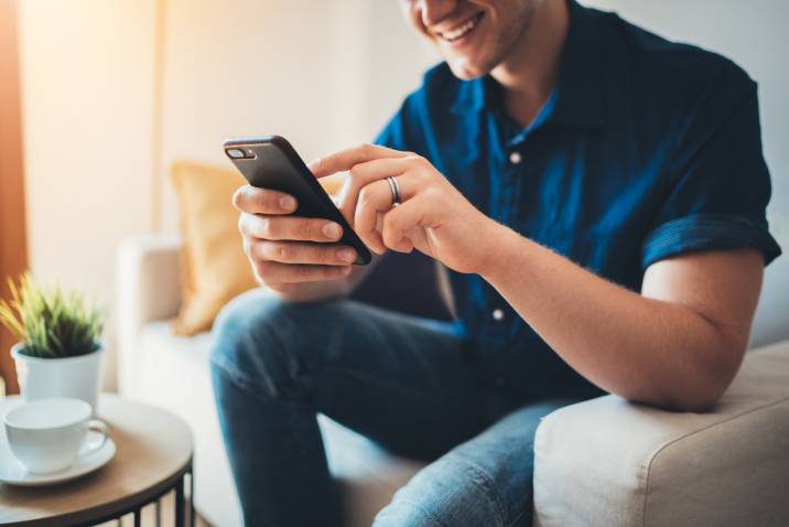 Happy smiling young man managing social media account on phone