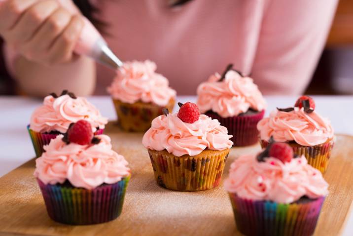 Closeup woman decorating raspberry cupcakes. Baking side hustle