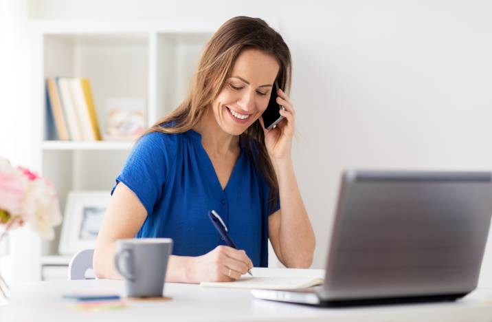 house sitter asking client questions over the phone while writing on notebook