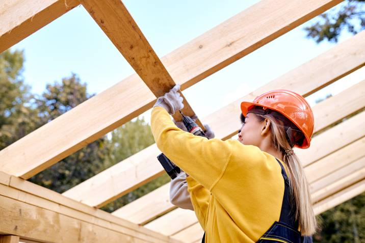 female carpenter working on roof section of wooden house skeleton