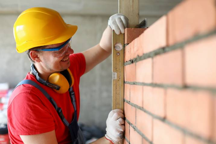 close-up of bricklayer using spirit level to check new red brick wall