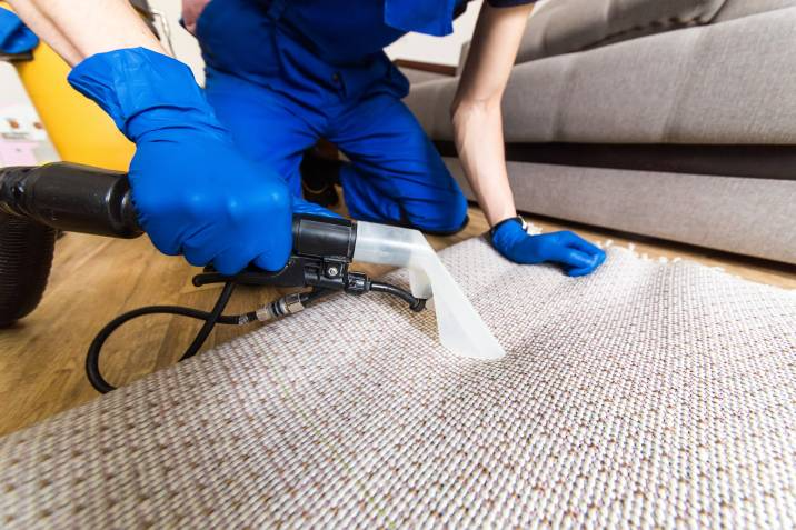 general labour, janitor in gloves and uniform vacuum cleaning white carpet with professional equipment