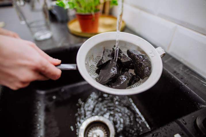 Woman cleaning small garden stones in sieve by pouring water in sink