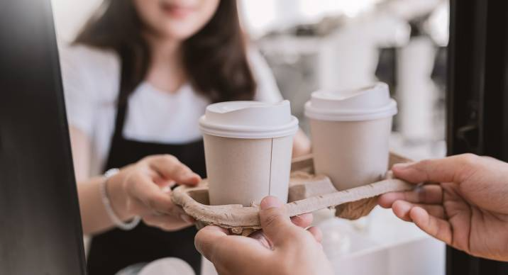 Close up woman hands gives paper coffee cup on slide glass window