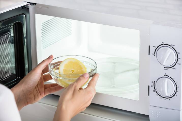 closeup hands, putting bowl of sliced lemon in microwave to clean and deodorise it