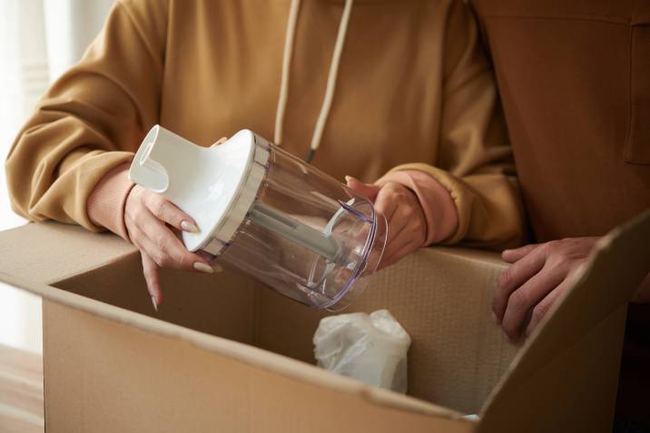 closeup hands, woman packing small kitchen appliance in moving box
