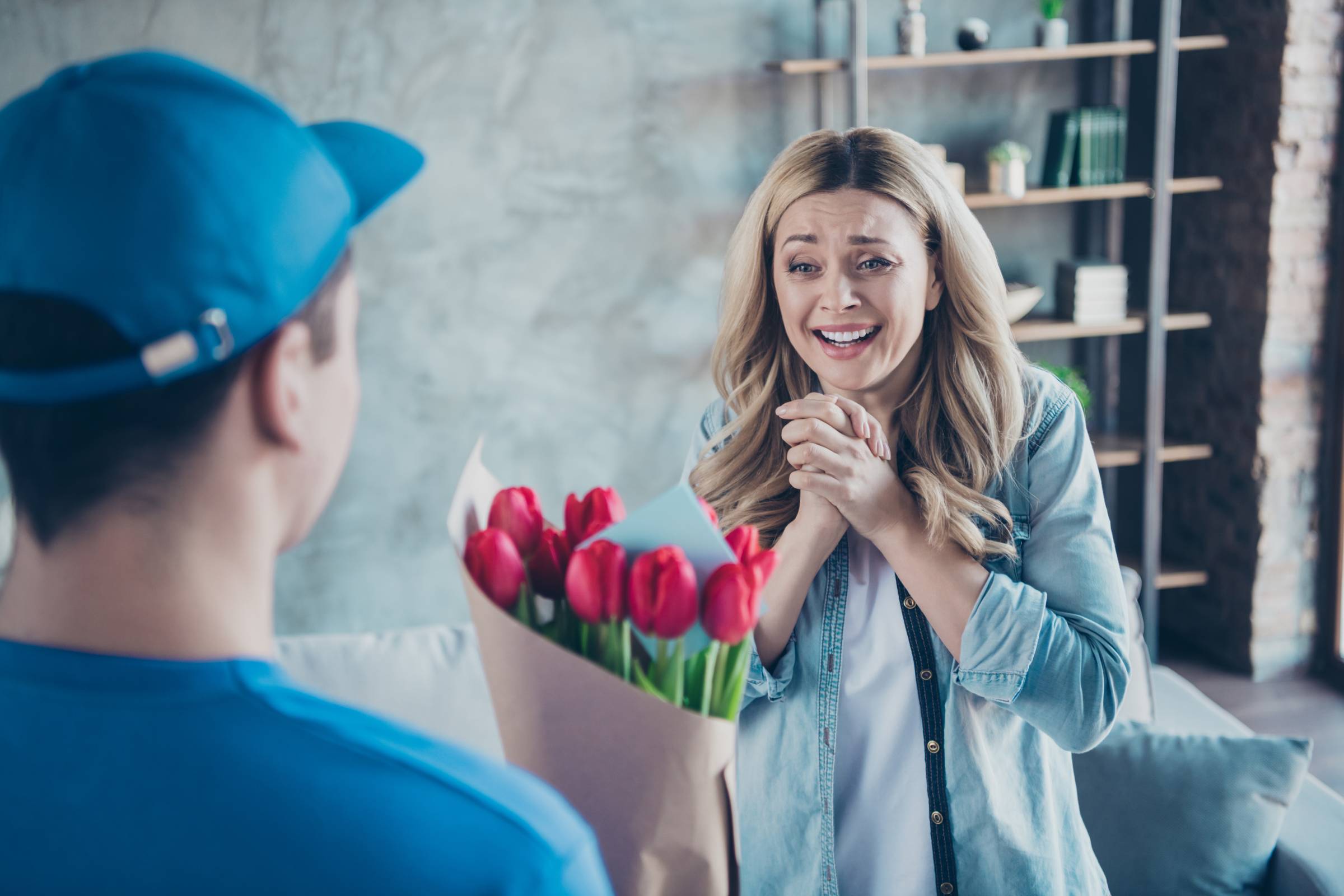 A woman joyfully receiving a bouquet of flowers from a delivery man in a blue shirt.