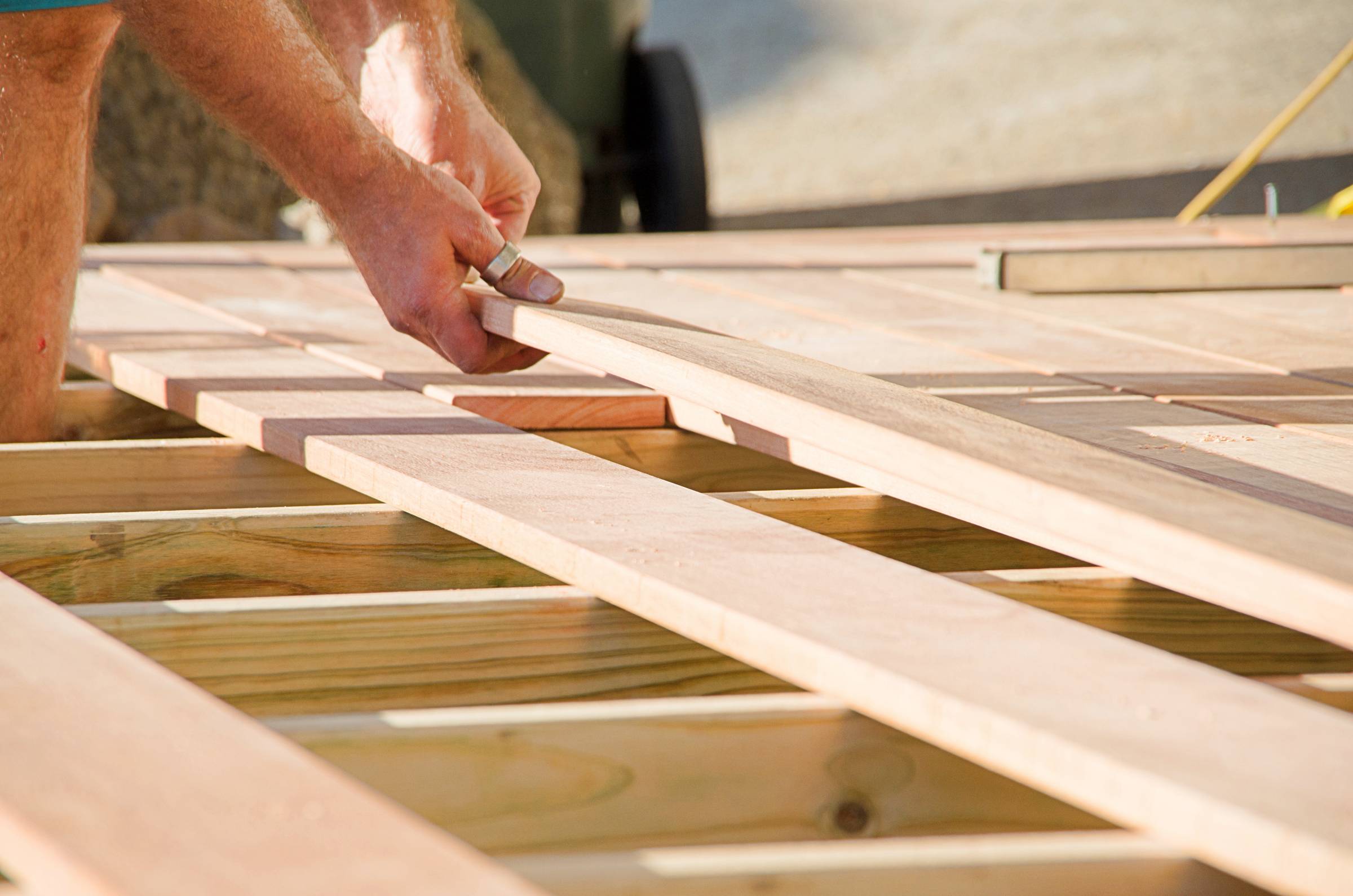 a man placing a plank of wood in a deck 