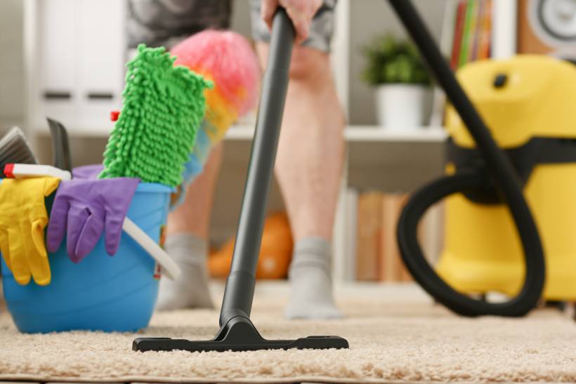 how to clean cat pee from carpet - a man vacuuming a carpet next to a bucket of cleaning tools