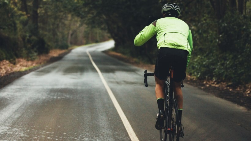 male athlete cycling on country road on rainy day to show what is a road bike