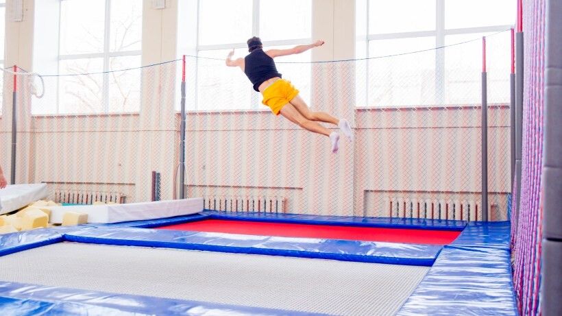 rectangle vs round trampoline: a portrait of happy guy jumping on a rectangle trampoline