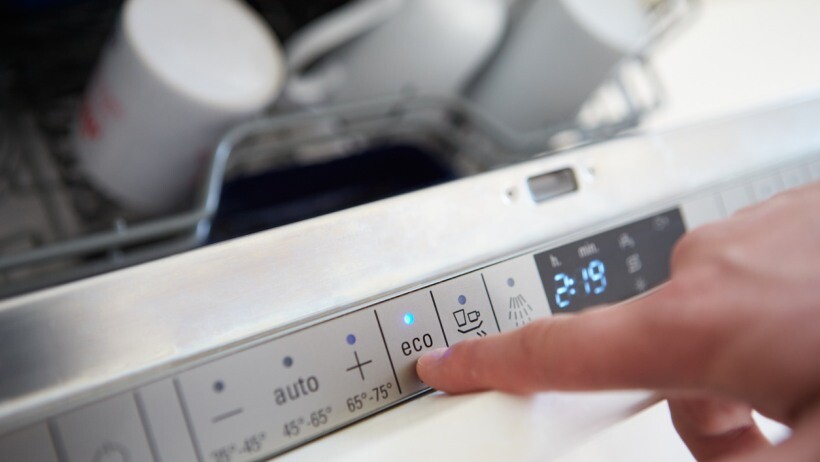 Integrated vs freestanding dishwasher: Close up of a person setting economy cycle on dishwasher