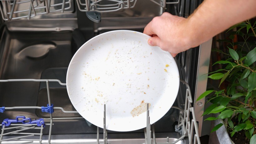 Dishwasher powder vs tablets - A person loads a dishwasher with dirty dishes.