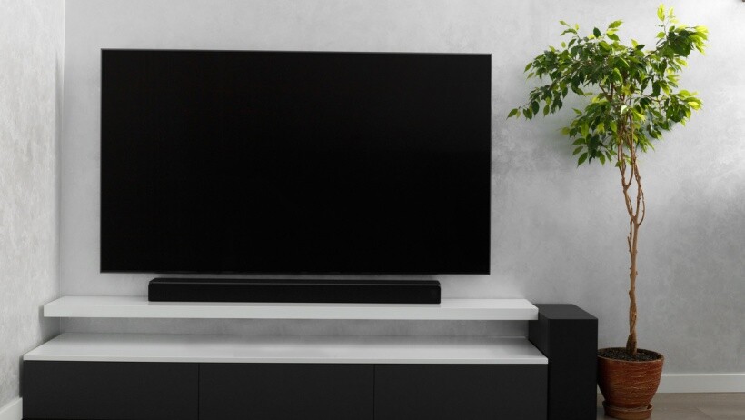 Soundbar vs surround sound - Part of the interior of the living room with a TV on the wall, sound bar, gray cabinet and a large indoor flower