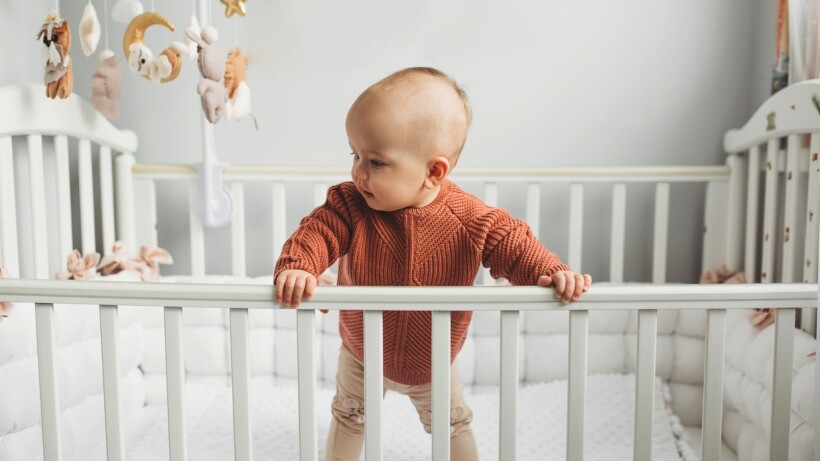 Bassinet vs cot - Adorable baby standing in a cot at home