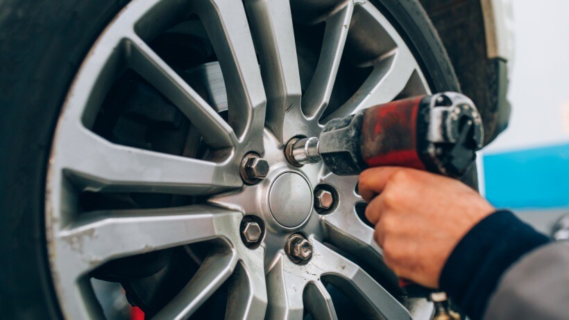 Impact driver vs impact wrench - A person adjusting a wheel using an impact wrench at the repair car garage 