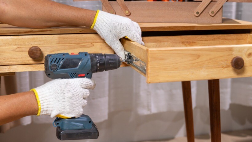 Impact driver vs impact wrench - A handyman repairing a wooden drawer of a cabinet using an impact drill