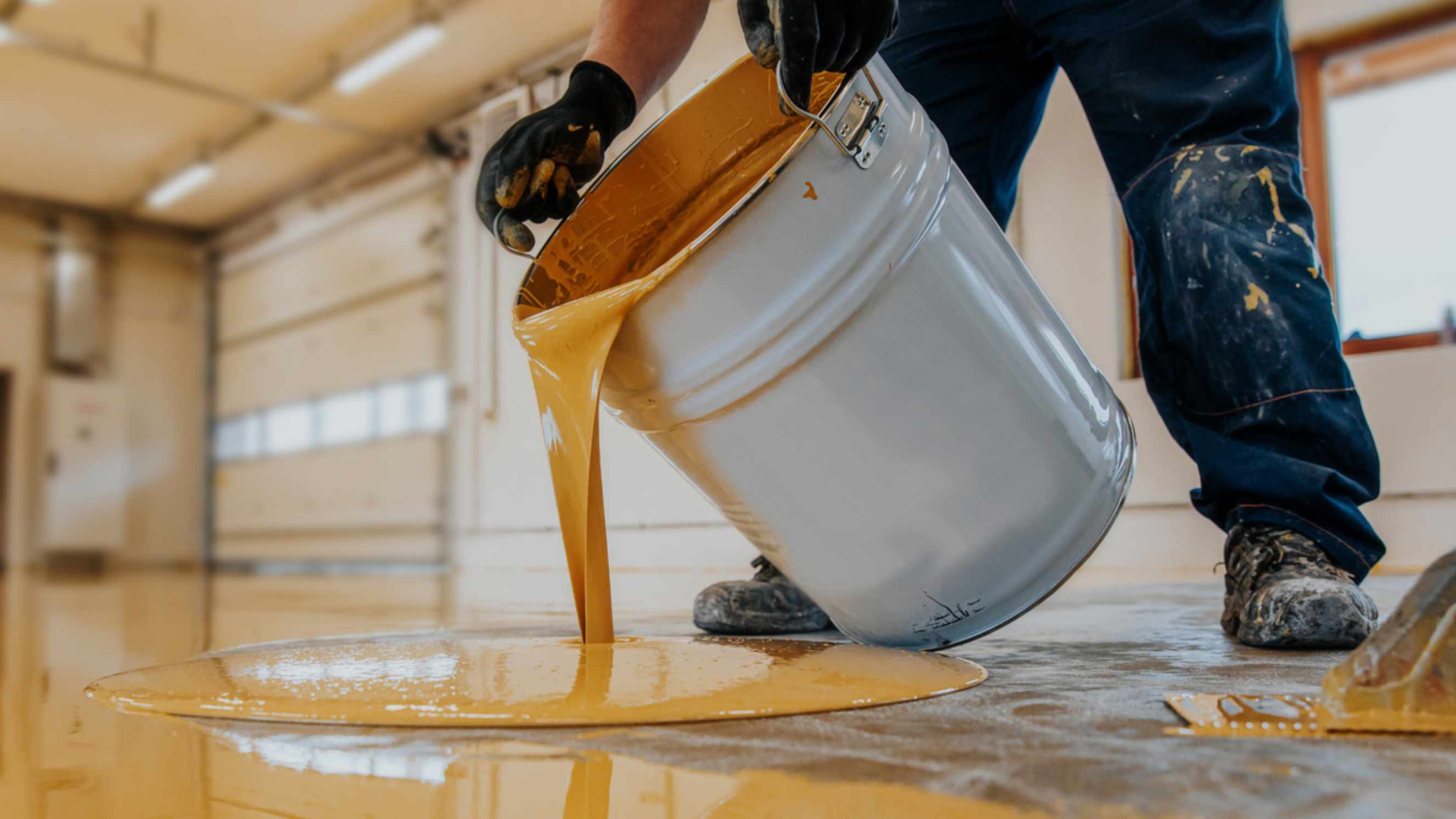 Polyester resin vs epoxy resin - A worker applying a yellow epoxy resin bucket on floor for the final coat