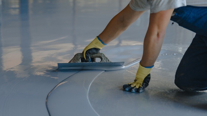 Polyester resin vs epoxy resin - A worker applying gray epoxy resin to a new floor