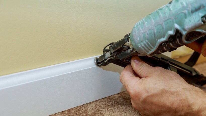 Brad nailer vs finish nailer - A handyperson using nail gun to base moulding trim