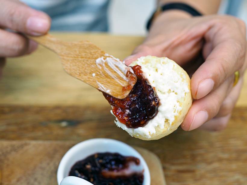 Devon vs Cornwall cream tea - a person spreading jam over clotted cream