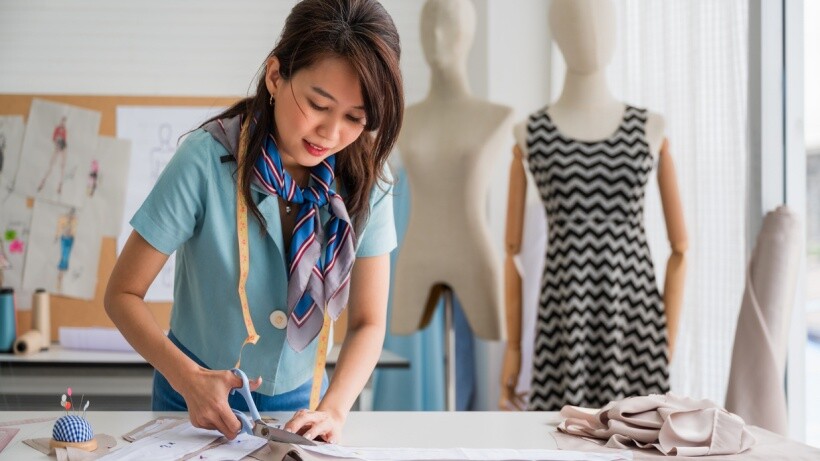 Seamstress vs tailor - A seamstress cutting fabric according to patterns in a fashion studio