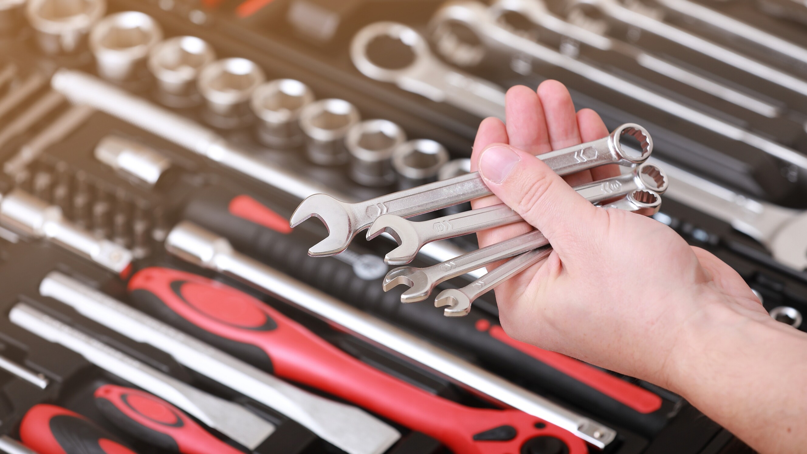 Spanner vs wrench - A man holding multiple wrenches from a repair tool kit.