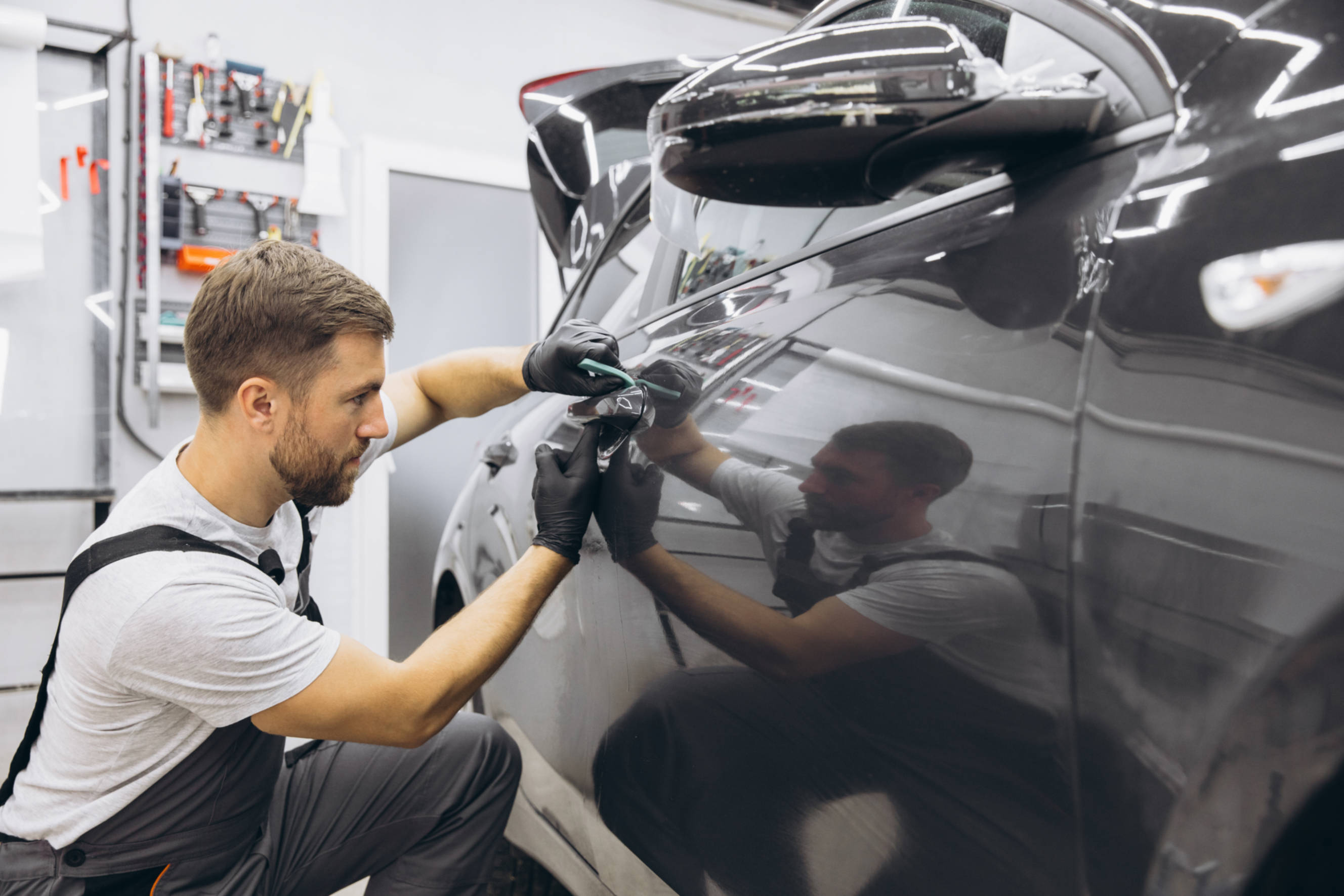 Technician applying vinyl film during a car wrapping service to protect and enhance the exterior of a vehicle in an auto workshop.