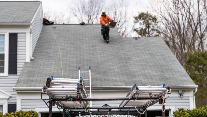 a man working on a house with grey roofing during winter - new roof cost