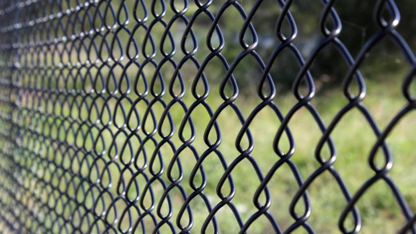 A detailed view of the intricate, wave-like pattern of a black metal fence against a blurred green background - fencing cost