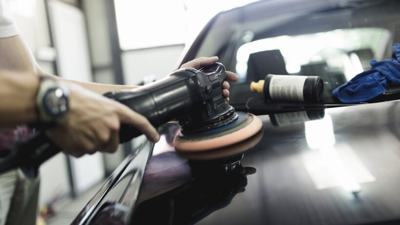 Car polish vs wax - A person's hands using a power polishing tool to buff and refine the finish on the exterior of a car in a garage or auto detailing setting