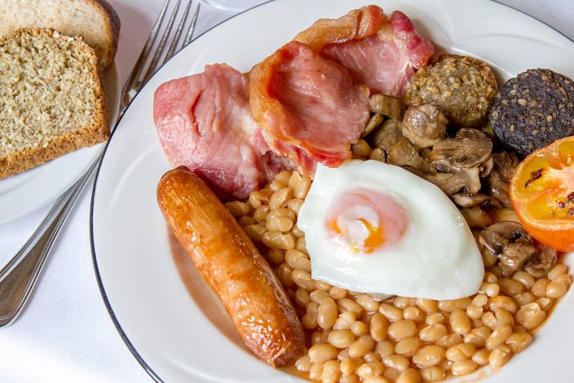 Irish breakfast vs English breakfast - a freshly prepared breakfast with eggs, baked beans, bacon, bread, tomatoes, and white and black pudding