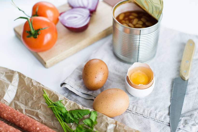 Irish breakfast vs English breakfast - English breakfast ingredients laid out on a table, including tomatoes, eggs, beans, onions, and sausage