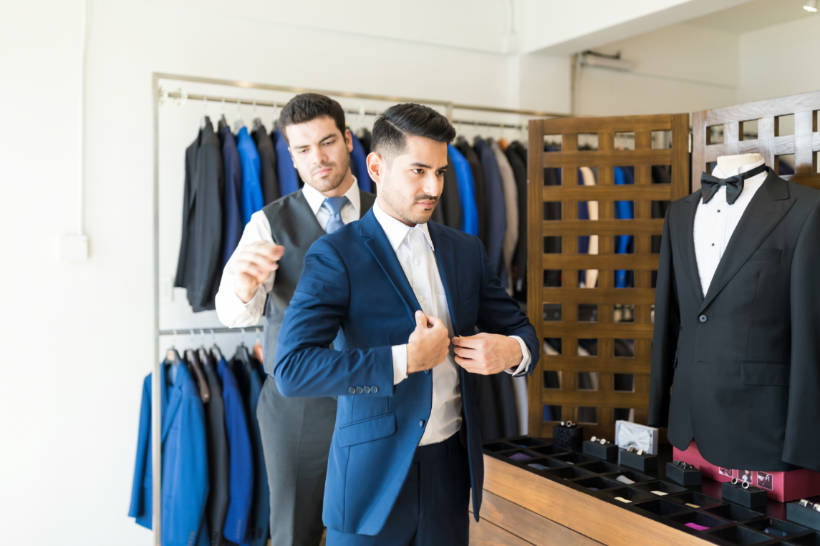 double breasted vs single breasted - tailor assisting a man in fitting a sleek, tailored blue suit with a modern silhouette