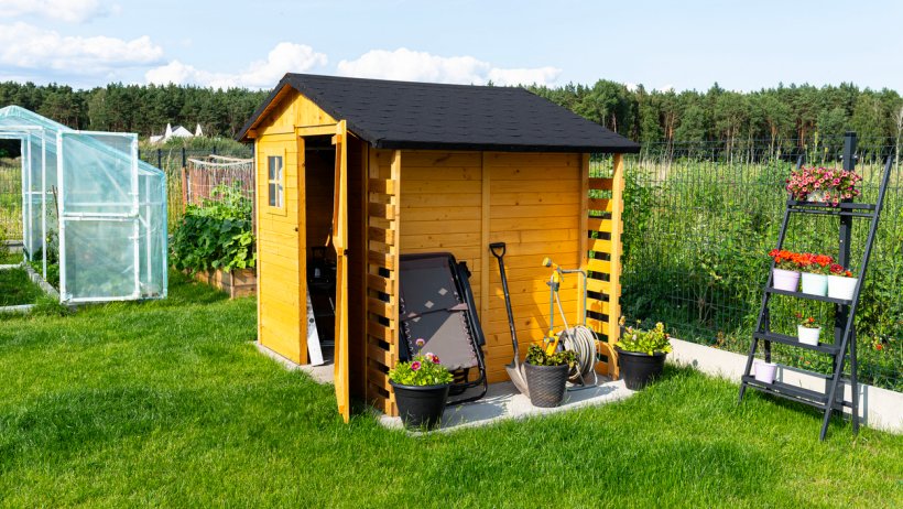  Wooden shed installed in a garden, surrounded by greenery, with gardening tools and equipment neatly stored