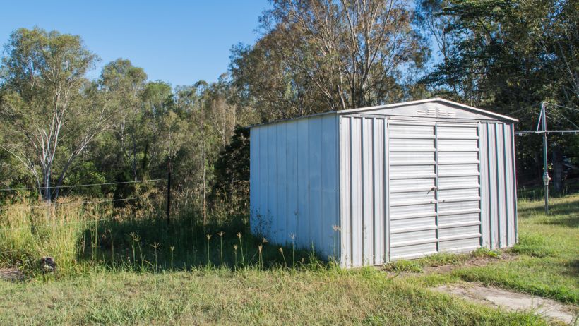 Steel shed in a backyard setting, surrounded by grass and trees