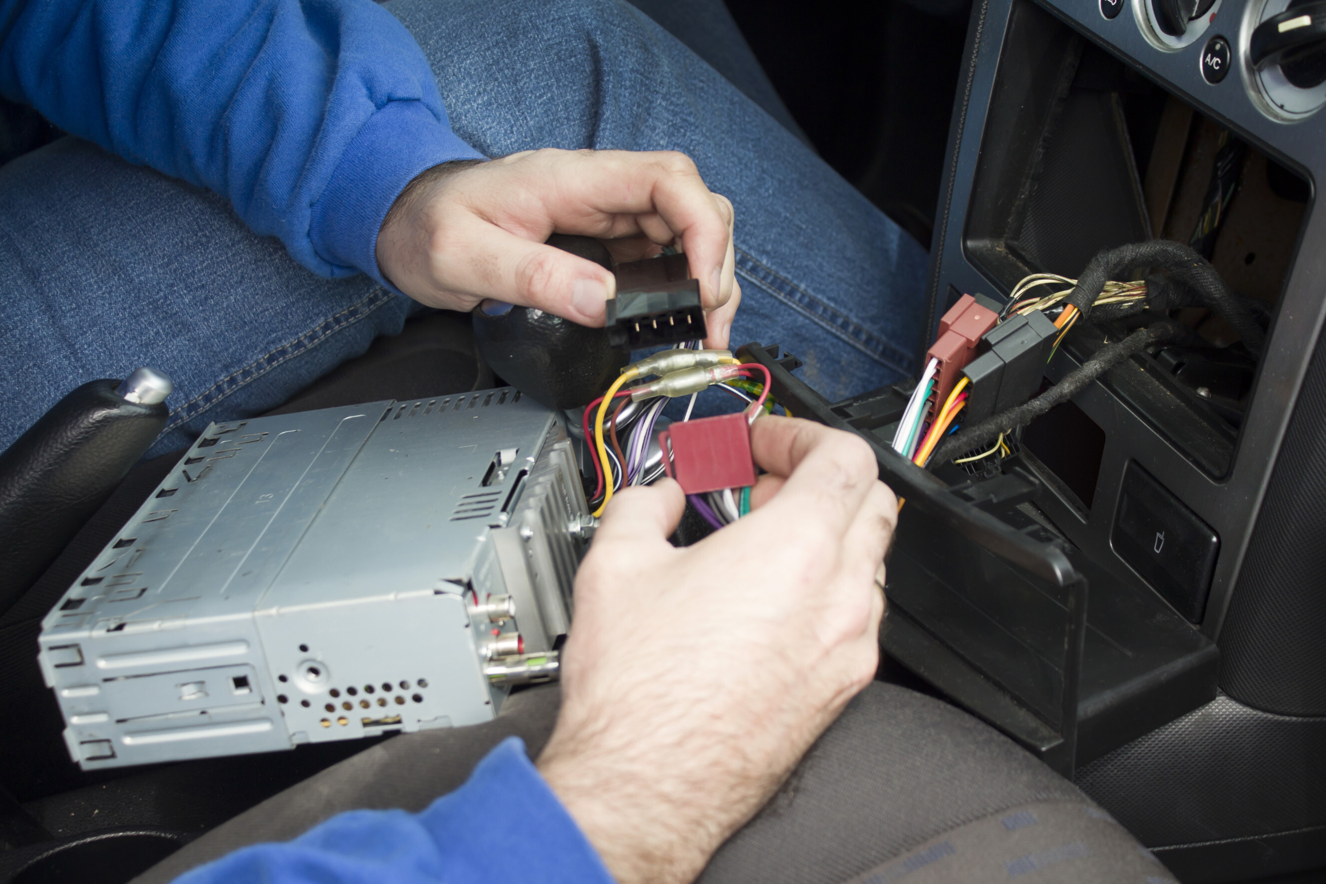 Auto electrician installing a car CD player and connecting wiring, highlighting professional CD player installation services near you.