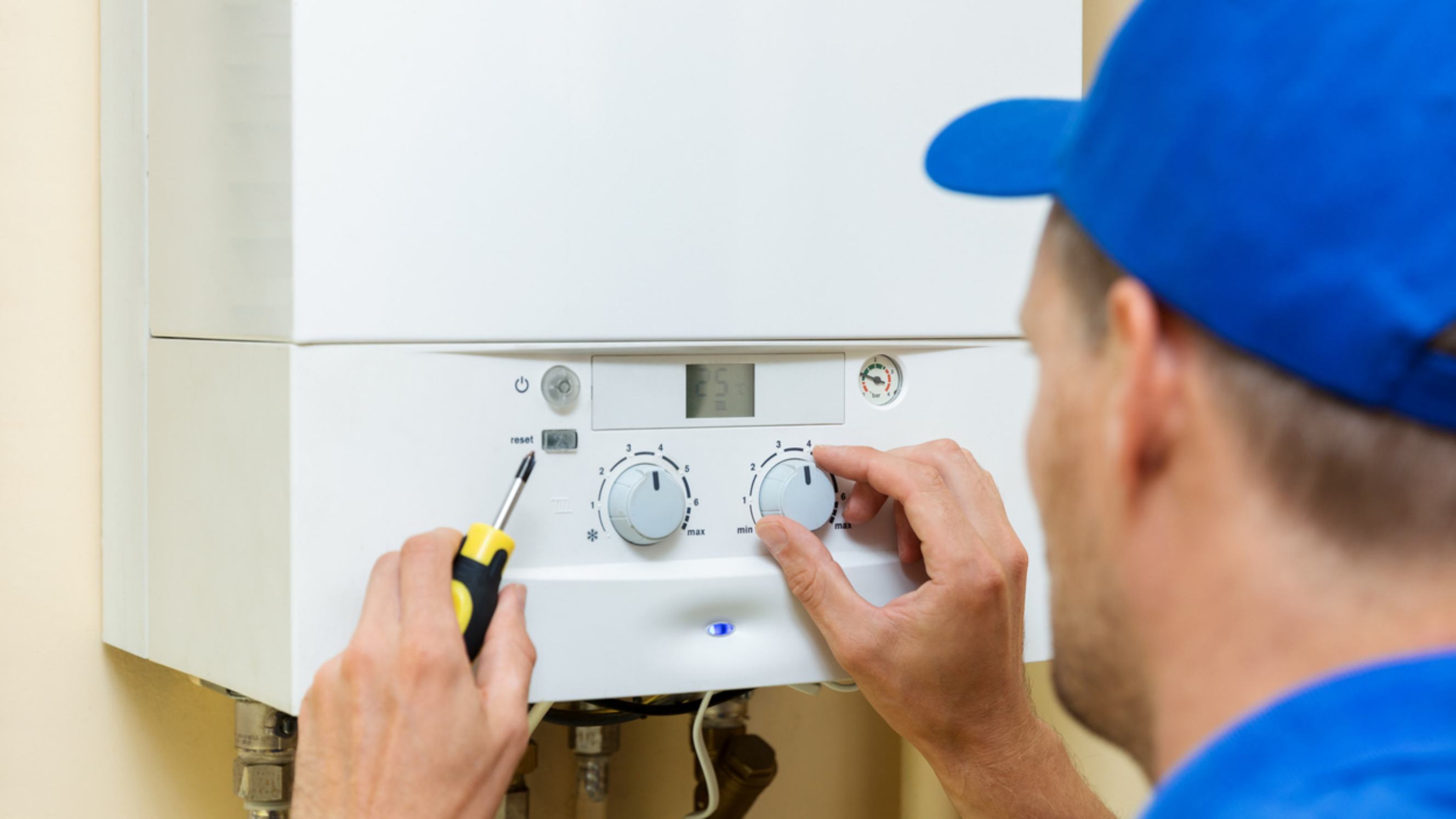 Electric boiler vs gas boiler - A technician wearing a blue cap adjusts the settings of a white boiler