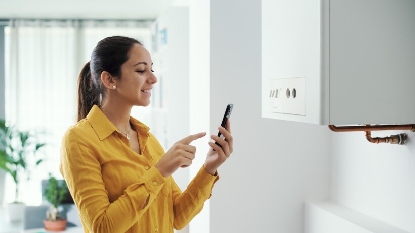 Electric boiler vs gas boiler - A woman in a yellow shirt smiling while adjusting her boiler settings using a smartphone