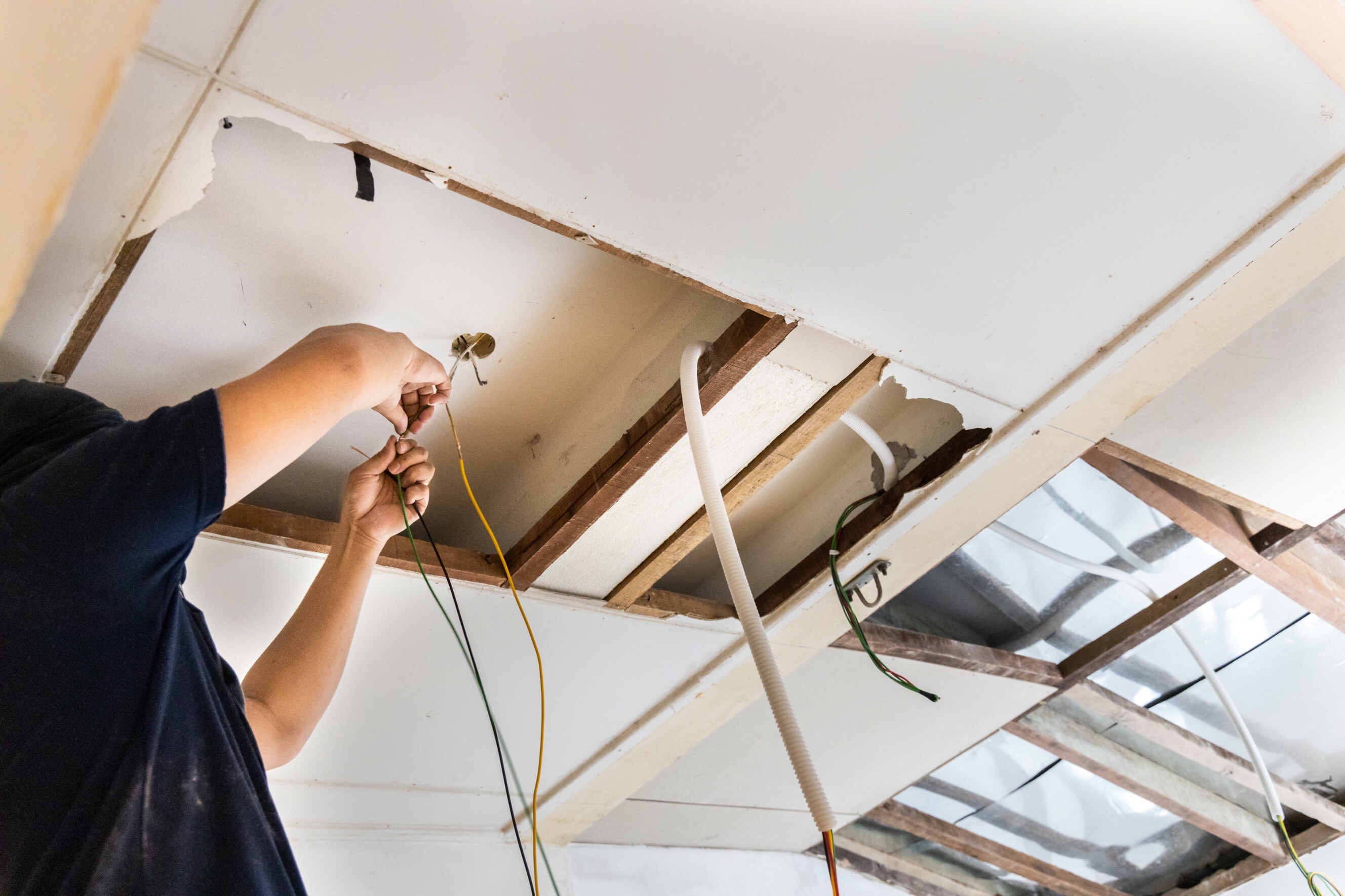 Electrician rewiring cables in a ceiling, highlighting professional electrical rewiring experts near you.