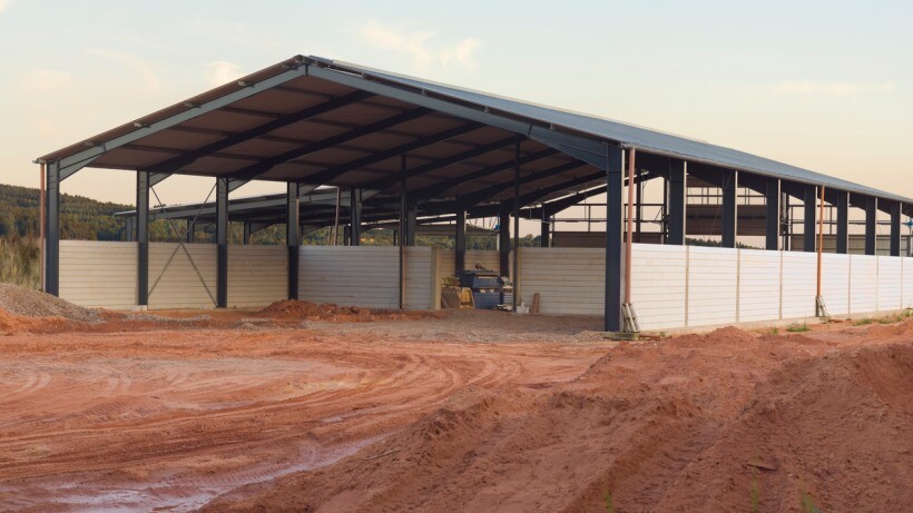 Barn vs shed - Large open-sided barn structure with a metal roof and partial walls, situated on a dirt surface