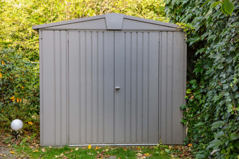 Metal vs wood shed — Metal shed surrounded by greenery in a backyard