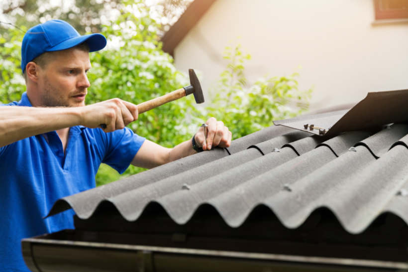 Metal vs wood shed — Man maintaining a shed roof with a hammer.