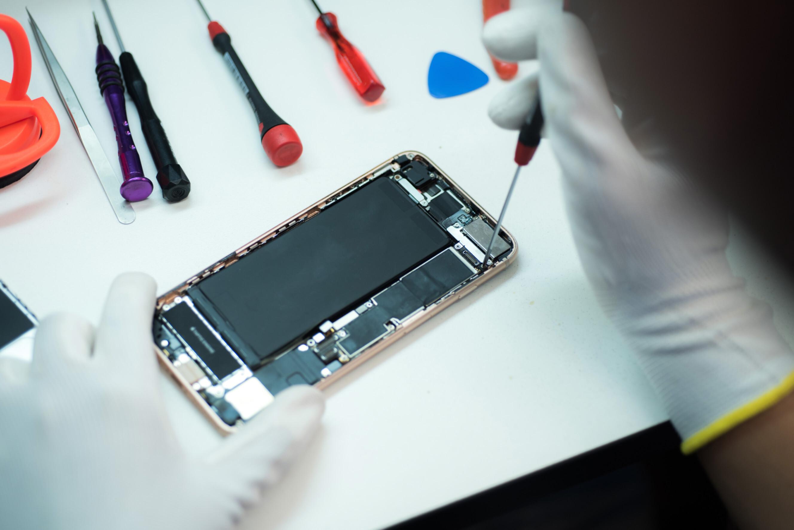 A professional iPhone technician wearing gloves carefully repairs an iPhone, using precision tools on a workbench with various repair instruments, representing expert iPhone help services near you.