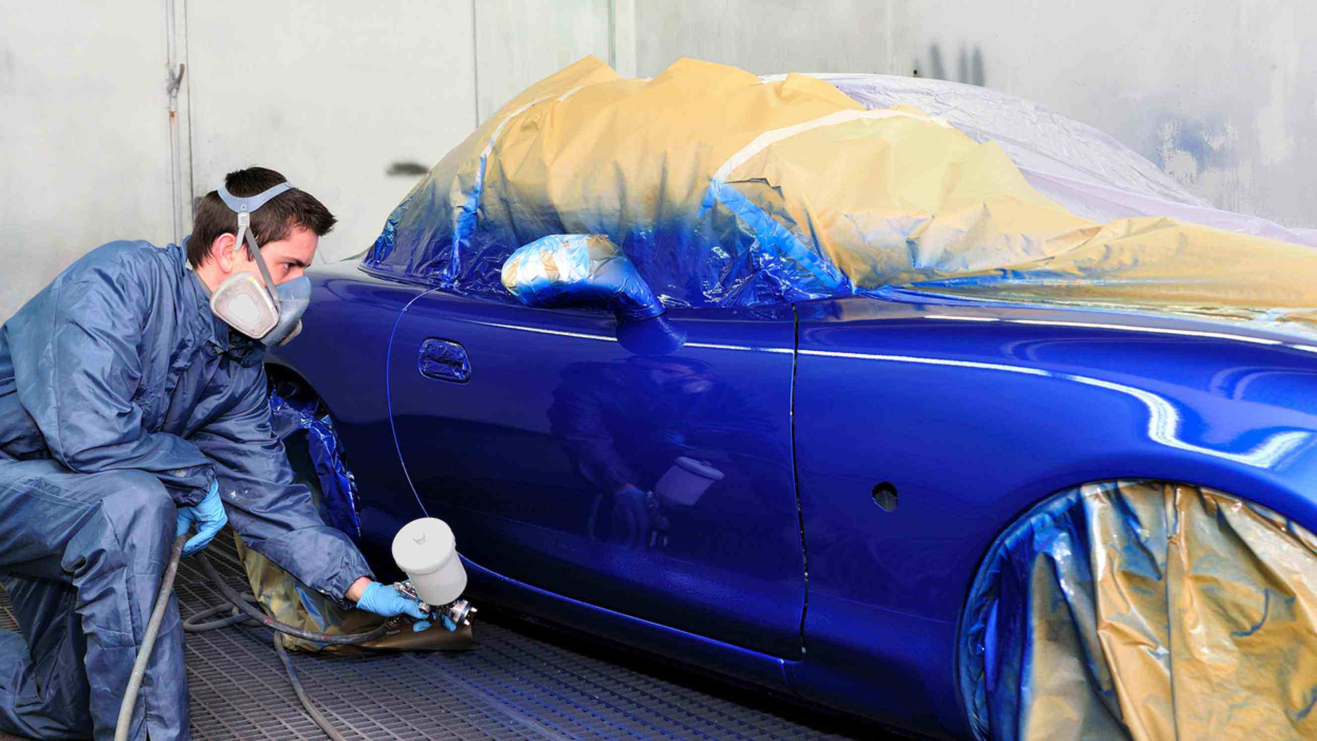 A professional applying a vibrant blue coat of paint to a car in a controlled spray booth, representing high-quality car paint services near you.