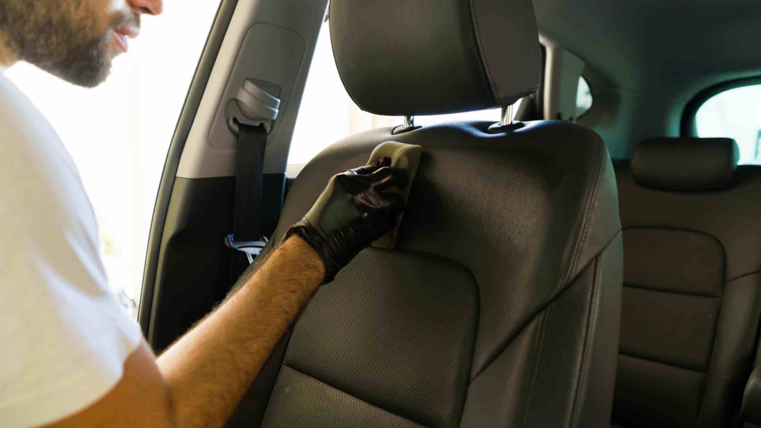 A professional technician wearing gloves carefully restoring a car's leather seat, representing reliable car seat repair services near you.